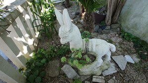 Un jardin agrémenté d’une sculpture en pierre représentant un lapin et un chien, entouré de verdure et de rochers.