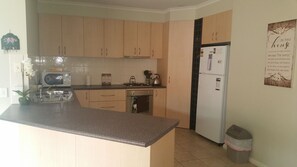 A kitchen with wooden cabinets, a refrigerator, a stove, and a trash bin.