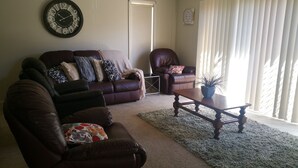 Uma sala de estar com um sofá de couro marrom, uma poltrona combinando, uma mesa de centro de madeira e um relógio de parede grande.