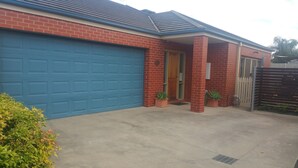 Uma casa residencial com porta da garagem azul, fachada de tijolos e varanda coberta.
