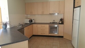 A compact kitchen with wooden cabinets, a microwave, a stove, and a dishwasher. - Annesley Central (Echuca)