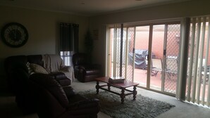 Uma sala de estar com sofá de couro, mesa de centro de madeira e porta de vidro deslizante que dá para um pátio externo.