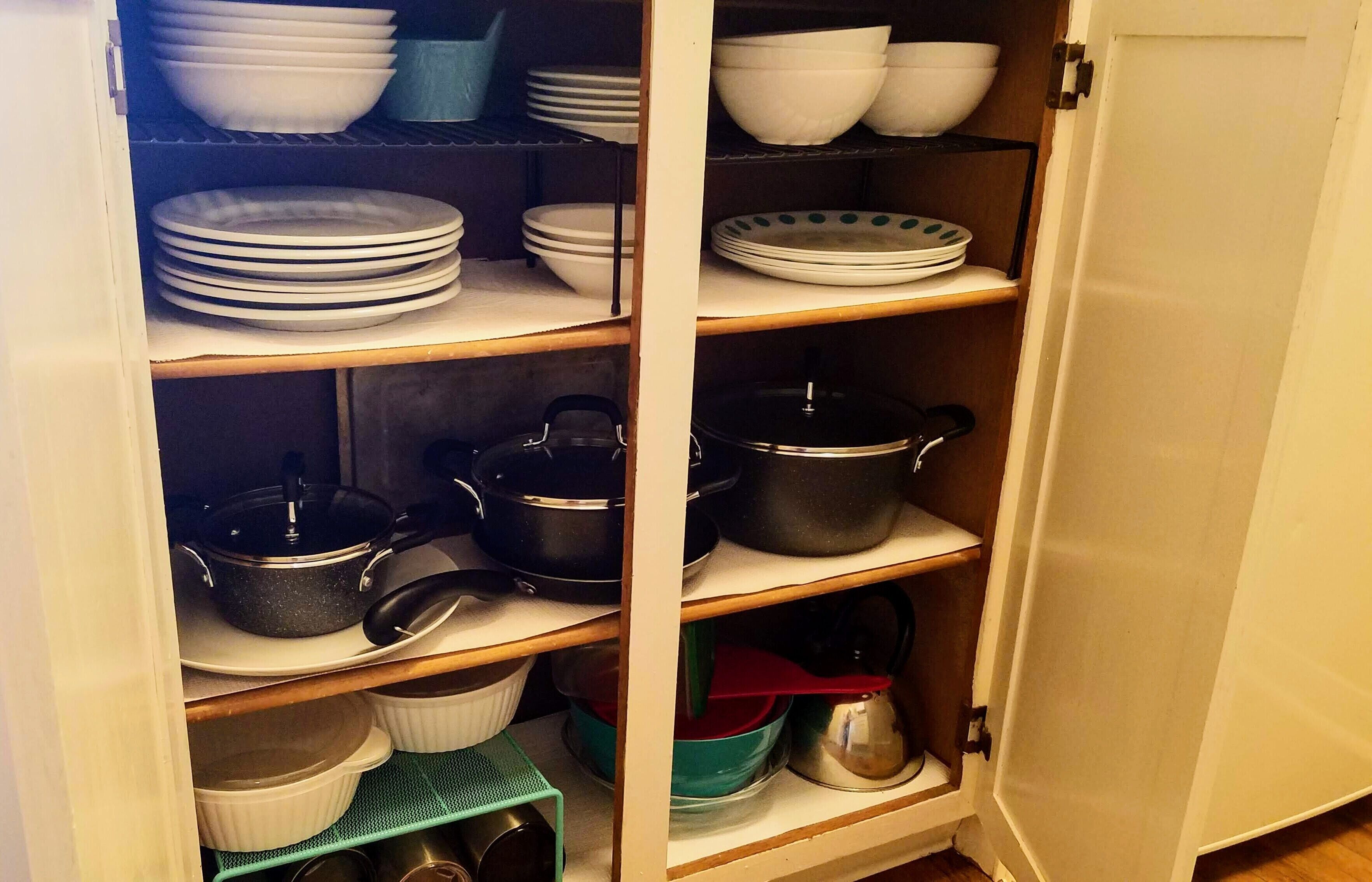 A kitchen pantry with shelves stocked with plates, bowls, pots, and kitchen utensils.