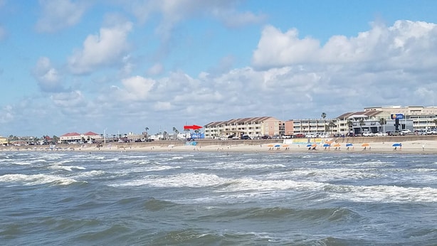 A beach with buildings in the background, a sandy shore, and waves in the foreground. - Beachfront condo near Top Places! Heated pool in Winter (Galveston)