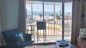 A room with a view of the beach, a blue sofa, a small table, and a brown couch. - Beachfront condo near Top Places! Heated pool in Winter (Galveston)