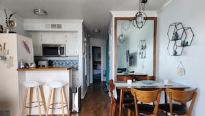 A modern kitchen with white cabinets, a wooden bar counter, and stools. There is a dining area with a wooden table and chairs. - Beachfront condo near Top Places! Heated pool in Winter (Galveston)