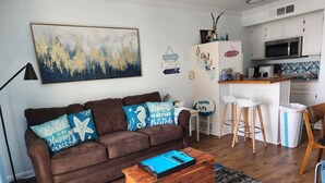 A living room with a brown sofa, blue cushions, a wooden coffee table, and a painting on the wall. - Beachfront condo near Top Places! Heated pool in Winter (Galveston)