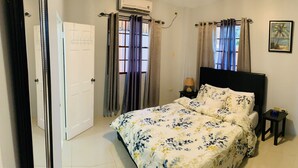 Een slaapkamer met een bed, gordijnen, een nachtkastje en een wandairconditioner.