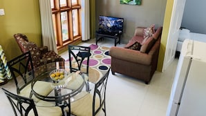 Een woonkamer met een televisie, bank, eettafel, stoelen en een raam met gordijnen.