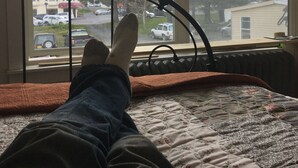 A bed with a metal headboard, a window with a view of a snowy mountain and a street with cars.