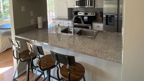 A modern kitchen with a granite countertop, stainless steel appliances, and a built-in island with bar stools.