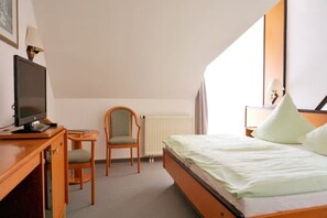 A hotel room with a bed, a desk with a television, a chair, and a radiator. - Hotel Stadt Zwönitz (Zwoenitz)