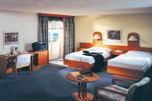 A hotel room with two beds, a desk, a chair, a small table, and a television. - Hotel Stadt Zwönitz (Zwoenitz)