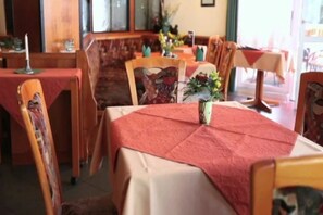 A restaurant interior with wooden chairs and tables, some with red tablecloths, and a vase with flowers on one table. - Hotel Stadt Zwönitz (Zwoenitz)