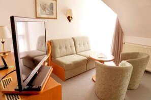A hotel room with a sofa, armchair, and a desk with a laptop. - Hotel Stadt Zwönitz (Zwoenitz)