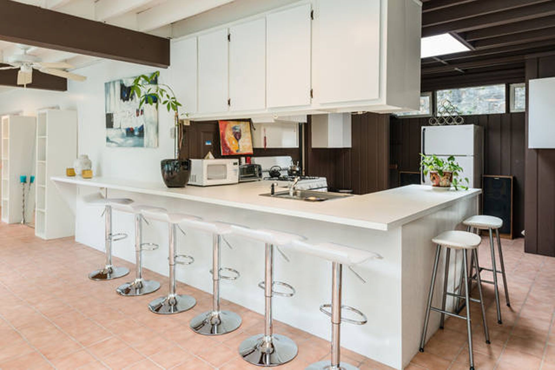 Une cuisine moderne avec des meubles blancs, un îlot central doté de tabourets et un four à micro-ondes.