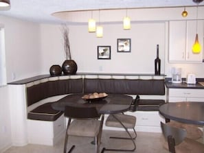 A modern kitchen with a built-in bench seating area, a round dining table, and pendant lighting. - Beachcomber unit 608 (Longboat Key)