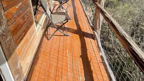 A wooden deck with a table and chairs, overlooking a natural landscape. - The Cedar House at Hamilton Creek (Burnet County)