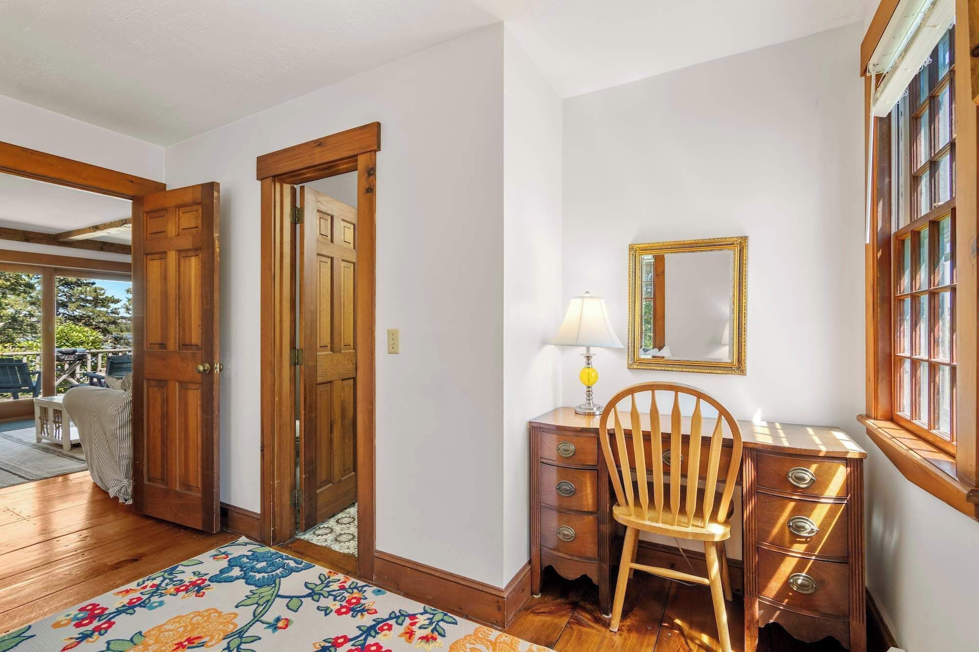 A room with a wooden desk, a chair, a lamp, a mirror, and a window.