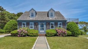 A two-story house with a blue exterior, a front porch, and a small deck on the second floor. - Stunning Water Views 2 Decks! By Beach! (Chatham)