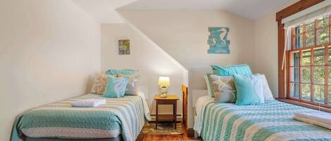 Un dormitorio con dos camas individuales, una mesita de noche con lámpara, una ventana con cortinas y un cartel náutico en la pared.