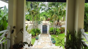 A stone pathway leading to a gated entrance surrounded by lush greenery and palm trees. - Mock Turtle is an Enchanting & Affordable Retreat! (Black Rock)