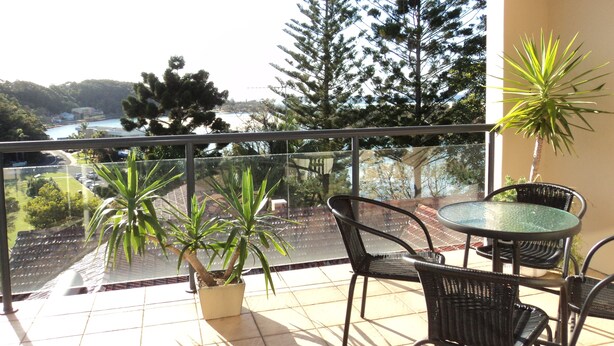 Un balcon avec une table et des chaises, des plantes en pot et une vue sur des arbres et une étendue d’eau.