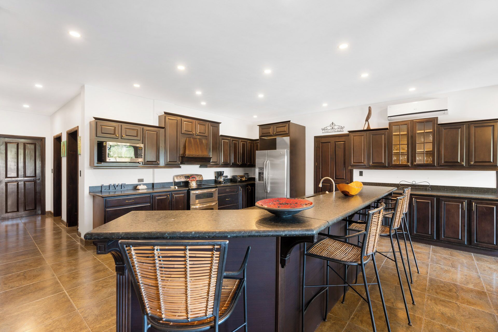 A modern kitchen with dark wood cabinets, stainless steel appliances, and a central island with bar stools.