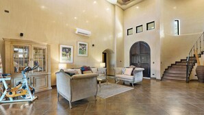 A spacious living area with a large sofa, a coffee table, a stationary bike, and a staircase leading to an upper level.