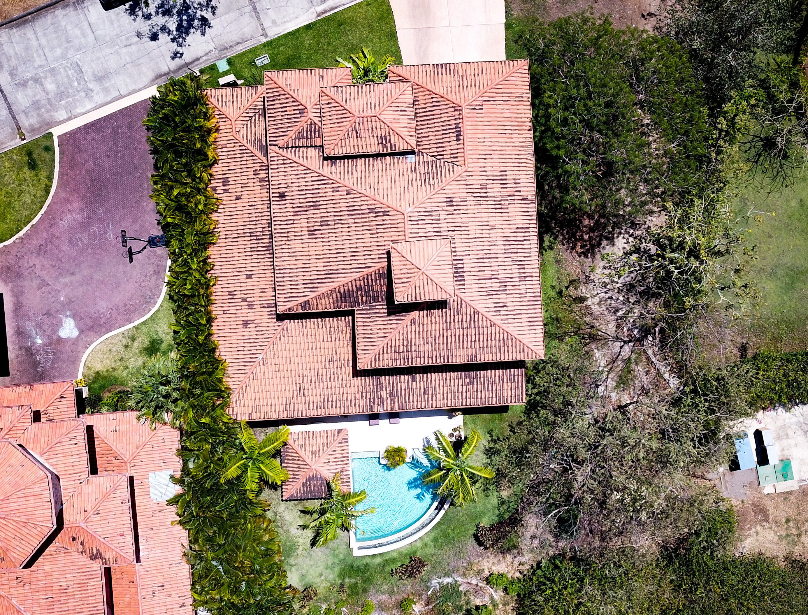 An aerial view of a property with a large swimming pool, a covered patio area, and a landscaped garden with palm trees.