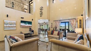 A spacious living area with a high ceiling, a dining area, and a view of the outdoors.