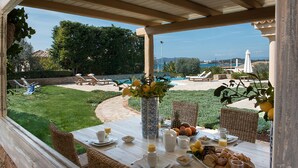 Un espace de restauration en plein air avec une table dressée pour le petit-déjeuner, donnant sur une piscine et un jardin.
