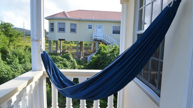 A balcony with a blue hammock, white balustrade, and a view of a house with a red roof. - YOUR HOME AWAY FROM HOME (Vieux Fort)