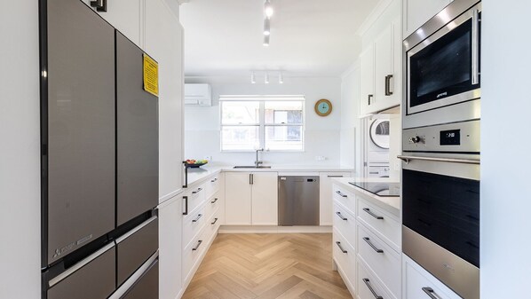 Une cuisine moderne avec des armoires blanches, des appareils en acier inoxydable et un parquet en bois disposé en motif chevron.