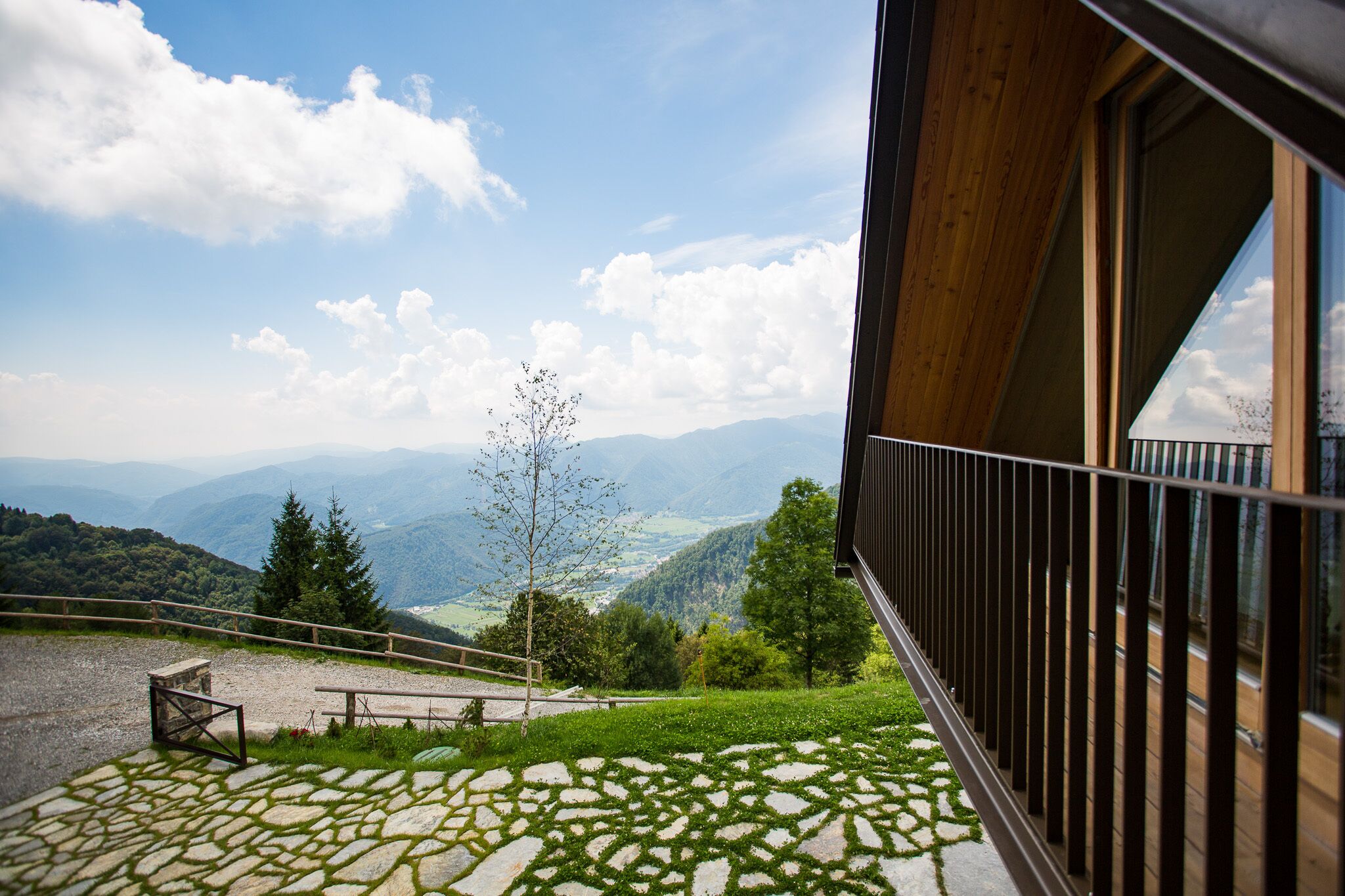 A balcony with a stone floor, a wooden railing, and a view of a mountainous landscape.