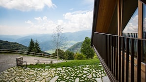 Un balcon doté d’un sol en pierre, d’une balustrade en bois et offrant une vue sur un paysage montagneux.