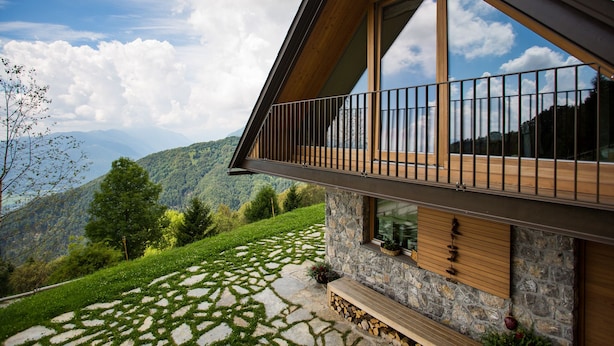 Une maison moderne avec une façade en pierre, de grandes fenêtres et un balcon donnant sur un paysage montagneux.