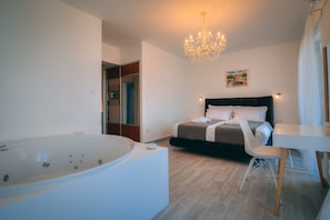 Relax in a serene bedroom with a bathtub, dark-colored bed, and elegant chandelier.