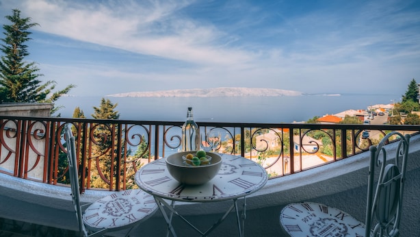A balcony with a table and chairs, a bowl of fruit, and a view of a distant cityscape. - Apartment **** "Lumin 4" 52 m2 (Senj)
