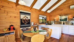 A wooden cabin interior with a dining area, kitchen, and a large window. - Siver Cabin (Kangaroo Valley)