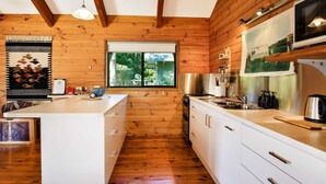 A modern kitchen with wooden walls, white cabinetry, and a large window. - Siver Cabin (Kangaroo Valley)
