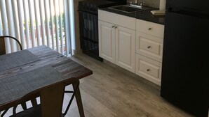 Een keuken met witte kastjes, een zwarte koelkast, een fornuis en een spoelbak.