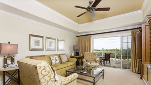 A spacious living room with a sofa, armchairs, a glass coffee table, and a ceiling fan. There are framed pictures on the wall and a view of the outdoors through a sliding glass door. - Modern Coziness: Orlando Apartment (Kissimmee)