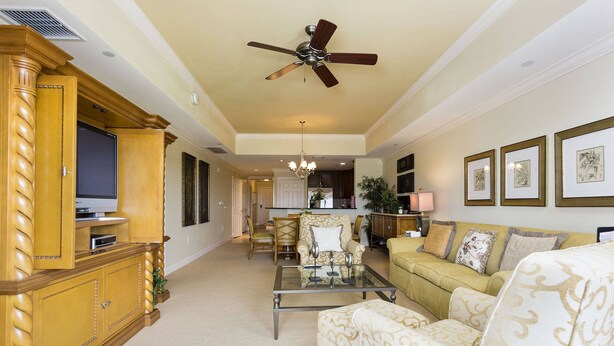 A spacious living room with a television, a ceiling fan, a dining area, and a kitchen in the background. - Modern Coziness: Orlando Apartment (Kissimmee)