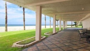 A covered outdoor area with a view of the beach, featuring a paved walkway and seating. - Beachcomber unit 405 (Longboat Key)