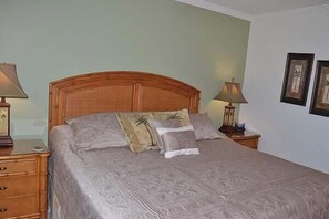 A neatly made bed with a wooden headboard, two bedside tables with lamps, and framed pictures on the wall. - Beachcomber unit 405 (Longboat Key)