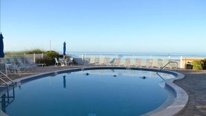 A swimming pool with a 7ft depth marker, surrounded by lounge chairs and umbrellas, with a view of the beach and ocean. - Beachcomber unit 405 (Longboat Key)
