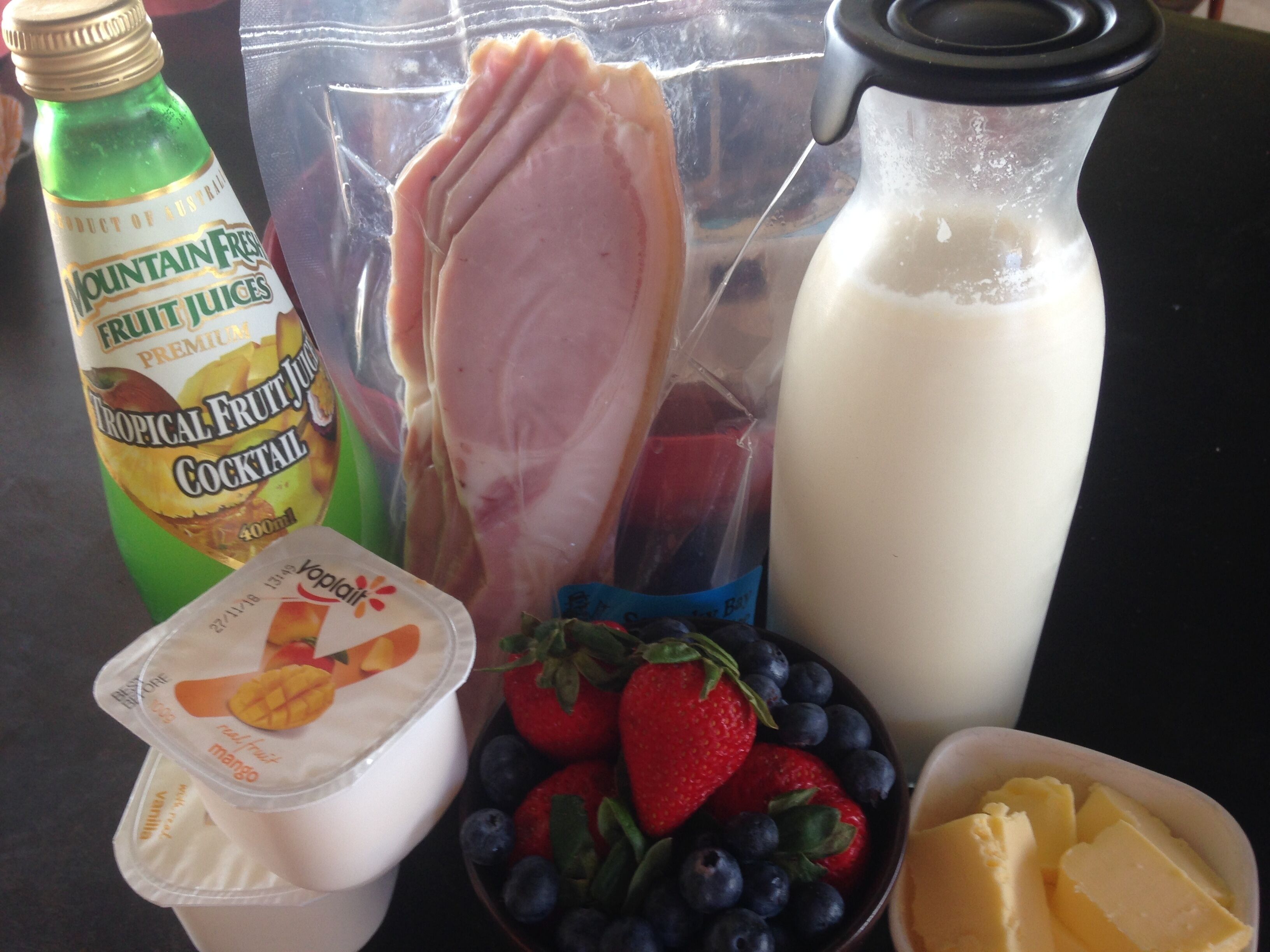 Une bouteille de cocktail de jus de fruits tropicaux « Mountain Fresh », un pot de yaourt, un bol de fraises et de myrtilles, un pot de beurre et une bouteille de lait.