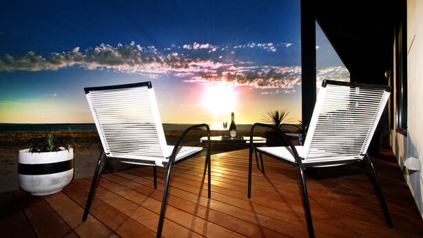 Zwei weiße Stühle mit schwarzem Gestell auf einer Holzterrasse, mit Blick auf den Sonnenuntergang.