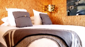 Ein Bett mit vielen Kissen und einer Decke, eine Holzwand und eine wandmontierte Leuchte.